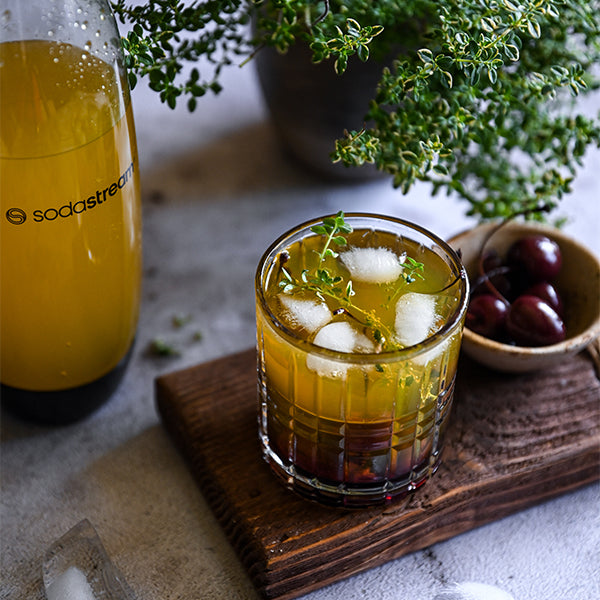 Drink bezalkoholowy „zachód słońca” z syropem pomarańcza-mango, tymiankiem i wiśniami