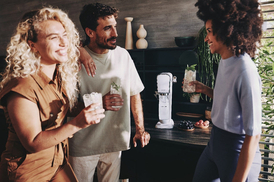 Trójka ludzi pije wodę gazowaną przygotowaną w saturatorze SodaStream na przyjęciu.