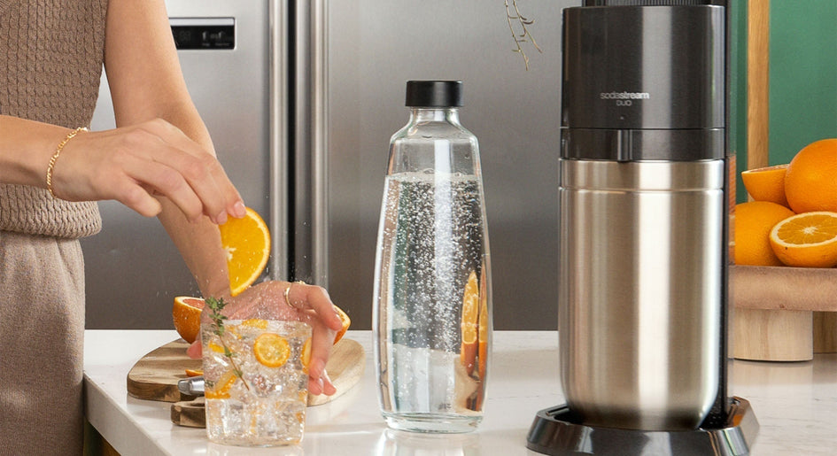 Kobieta przygotowująca wodę gazowaną z pomarańczą i ekspres do wody gazowanej SodaStream Duo