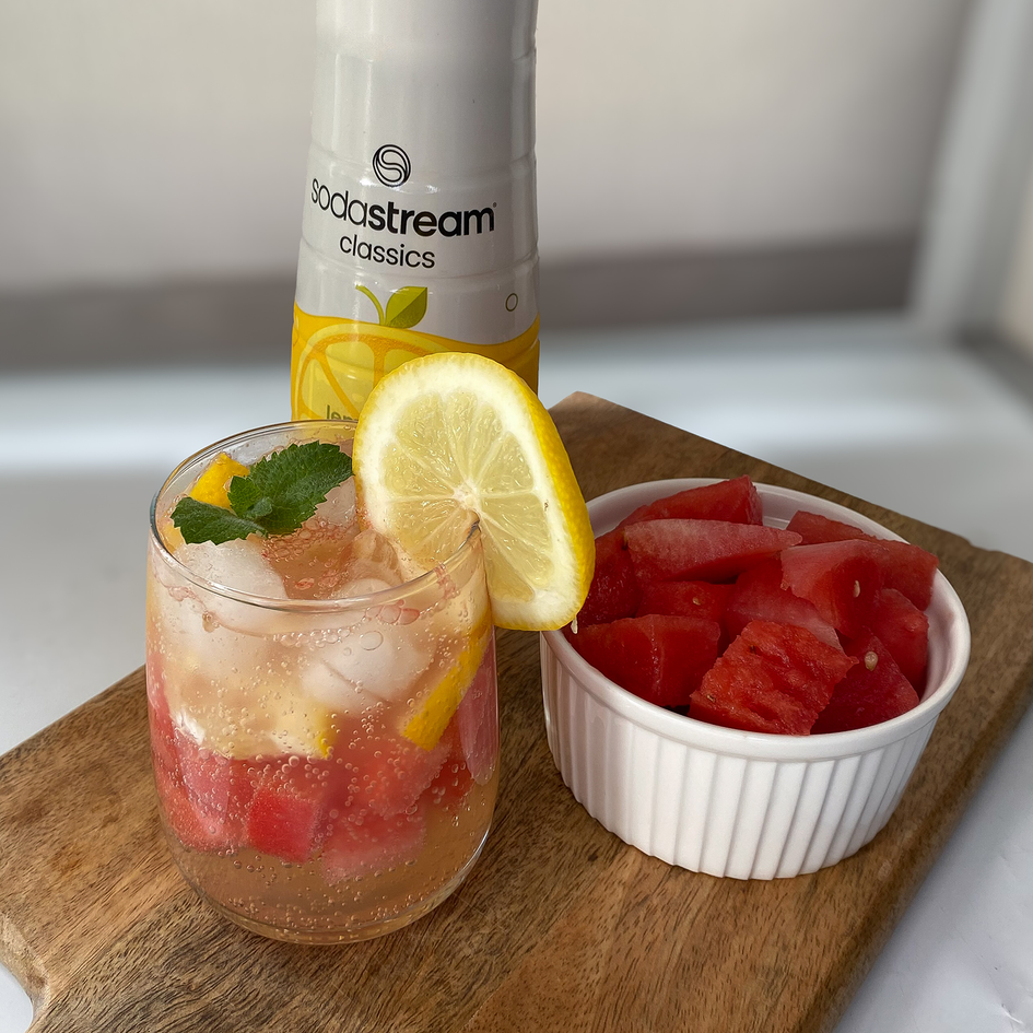 Orzeźwiający drink bezalkoholowy cytryna-arbuz z butelką syropu Lemoniada SodaStream na drewnianej desce do krojenia