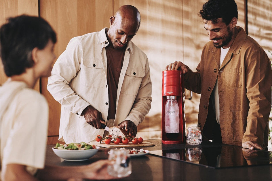 Mężczyźni przygotowują wodę gazowaną w saturatorze SodaStream Terra w kolorze czerwonym na przyjęcie zero waste. 