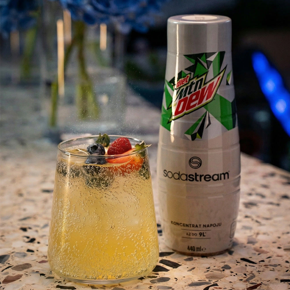Szklanka gazowanego napoju z owocami obok syropu SodaStream Mountain Dew na blacie. - zdjęcie