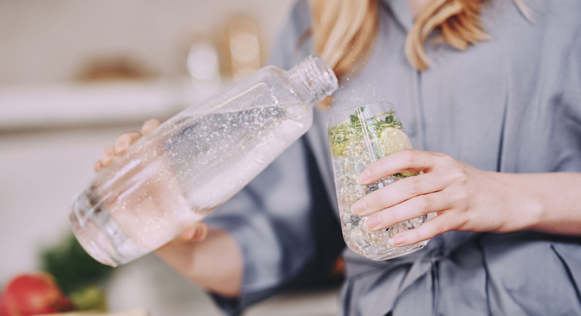 Kobieta przelewająca wodę gazowaną z butelki do szklanki z lodem i dodatkami