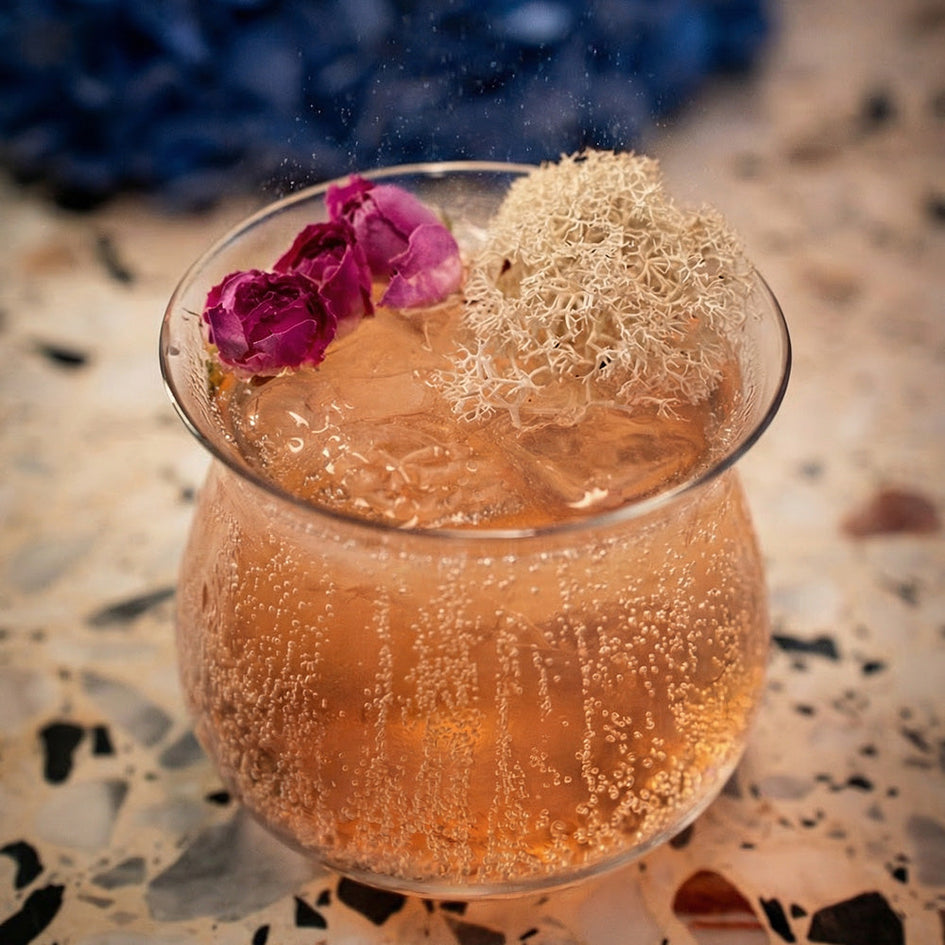 Szklanka różowego, gazowanego napoju z lodem i dekoracją z kwiatu na jasnym blacie. - zdjęcie