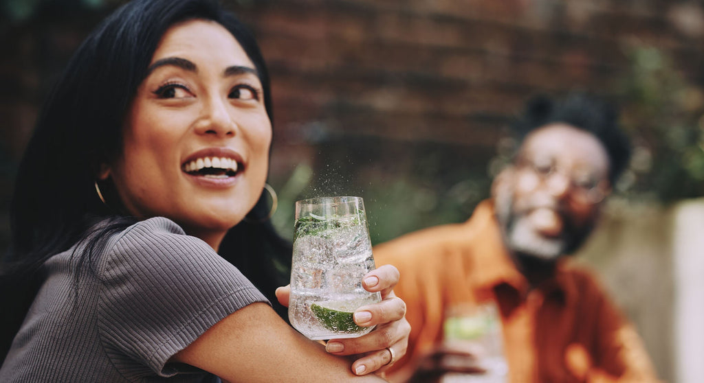 Uśmiechnięta kobieta trzymająca szklankę z wodą gazowaną i dodatkami 