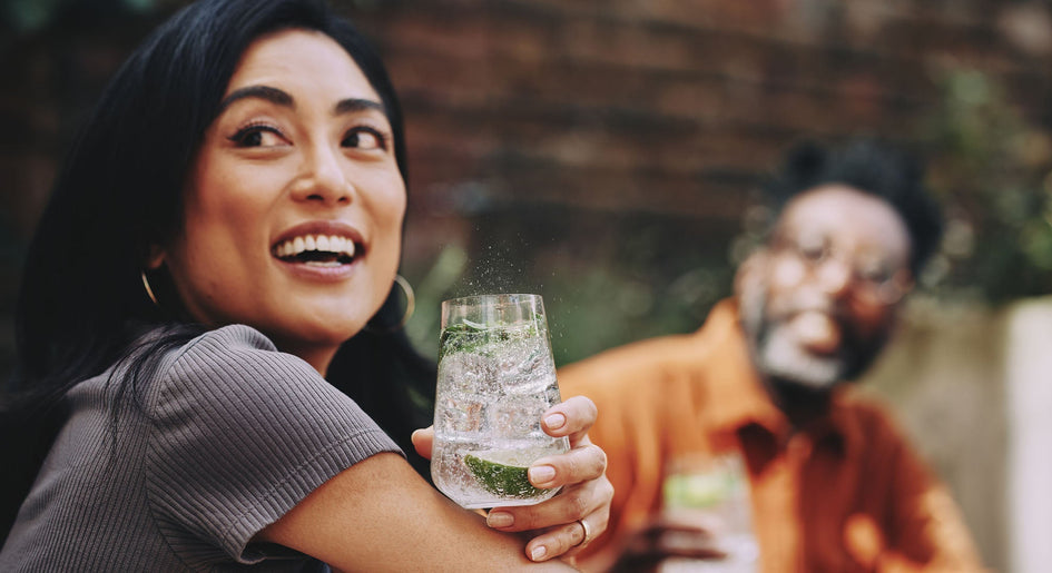 Uśmiechnięta kobieta trzymająca szklankę z wodą gazowaną i dodatkami 