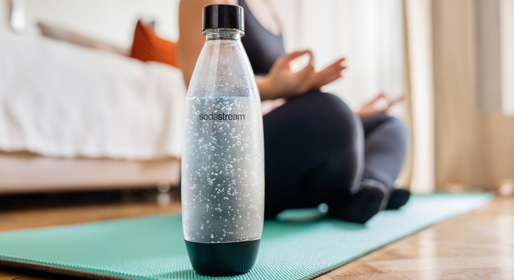 Butelka SodaStream z wodą gazowaną i kobieta podczas jogi