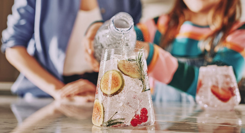 Matka z córką nalewający wodę gazowaną SodaStream do szklanki z dodatkami