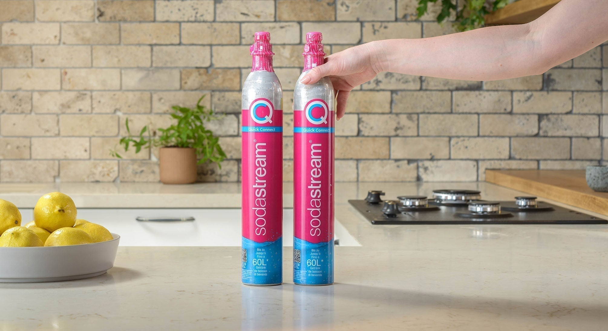  Ręka sięgająca jeden z dwóch stojących na blacie cylindrów do saturatora SodaStream