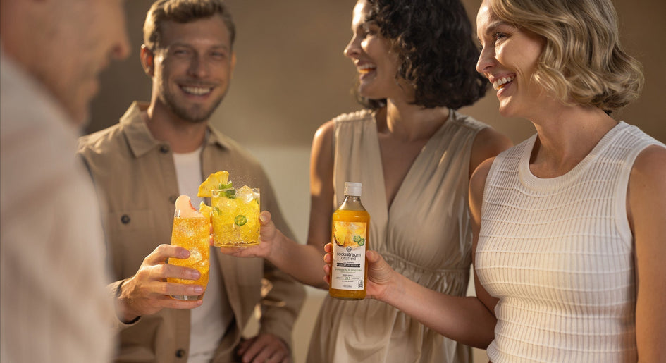 Grupka uśmiechniętych przyjaciół przy mocktailach z syropem SodaStream crafted.